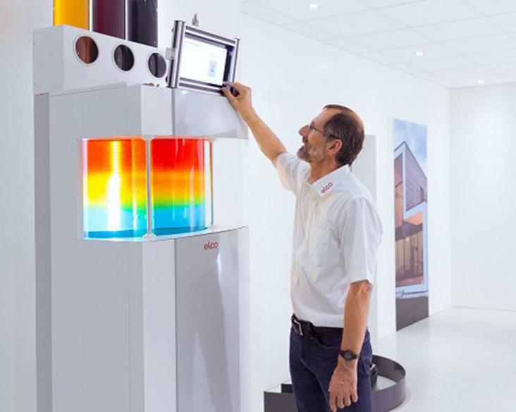 O persoană demonstrează într-un showroom un sistem de încălzire ELCO cu panou de control digital și afișarea vizuală a distribuției căldurii.